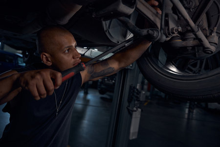 Focused African American auto-mechanic checking condition of car chassis