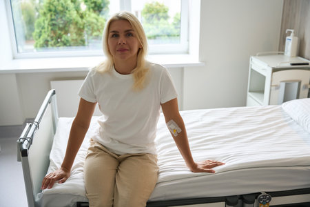 Patient sits on a hospital bed in a bright roomの写真素材