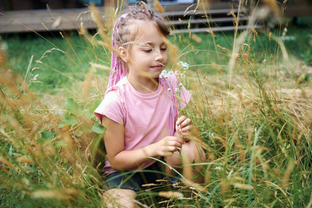 Pretty girl sitting on grass and collecting small wildflowersの写真素材