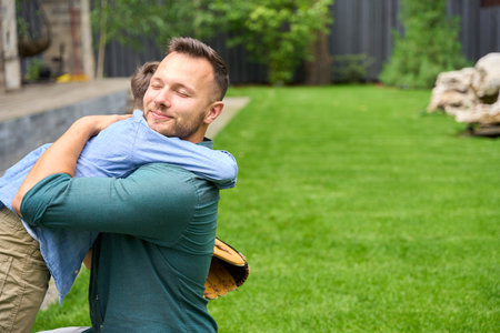Smiling father hugs son on green lawnの写真素材