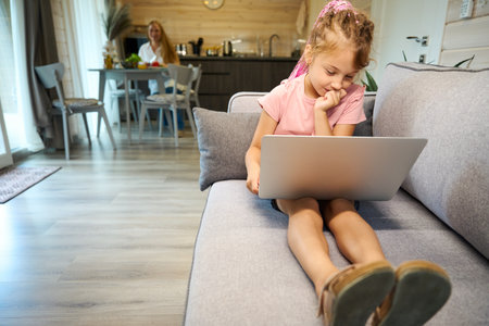 Cute girl studying online, sitting on sofa with laptopの写真素材