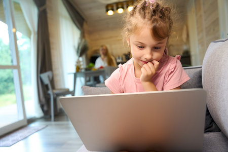 Clever little girl looking at laptop display sitting on sofa