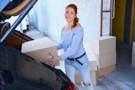 Smiling woman tooka cardboard box from the trunk of car