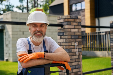 Pleased construction worker in hard hat posing for camera on siteの写真素材
