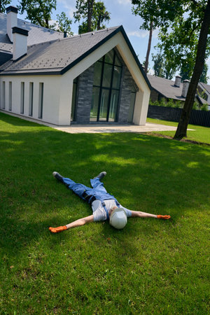 Builder resting on lawn in yard outside newly built houseの写真素材