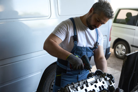 Professional automotive mechanic is repairing vehicle engine in his garage