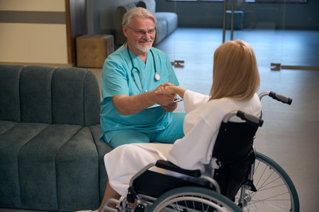 Friendly male doctor greeting disabled patient with handshake in hospital foyerの写真素材