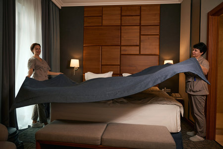 Team of skilled hotel maids busy with bed-making in guest suite