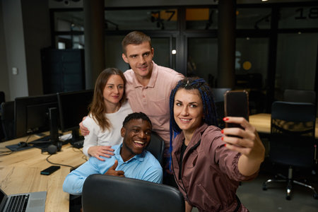 Multiethnic team gathering near working place in office and making selfieの写真素材