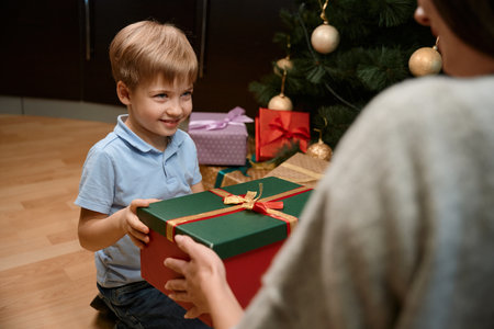 Little boy celebrates Christmas with mother sharing presents near the X-mas treeの写真素材