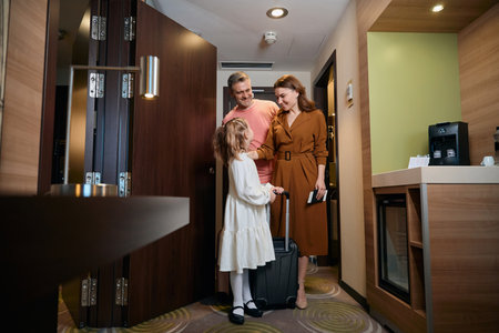Family of mother, father and daughter with suitcase entering hotel roomの写真素材