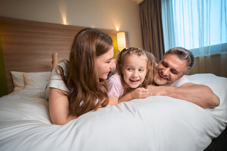 Mother, father and daughter lying and resting on bed in hotel roomの写真素材