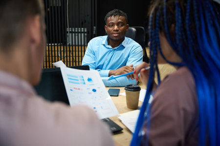 African American company leader listening to report of his caucasian colleagues