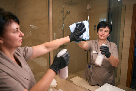 Uniformed chambermaid is cleaning hotel bathroom fixturesの写真素材