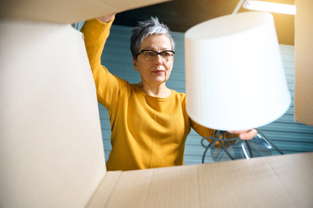 Woman taking lamp out of moving boxの写真素材