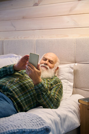 Pensioner is tired and lies down to rest on cozy bedの写真素材