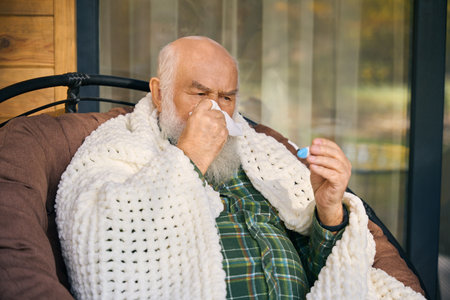 Sick old man is wrapped in fluffy blanket on verandaの写真素材
