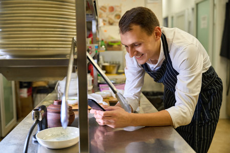 Cook at the kitchen rack communicates on his mobile phone