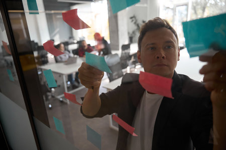 Business man looking through memo notes stickered to the transparent wall
