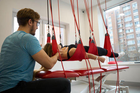 Male rehabilitologist fixes a woman in a suspension loop system