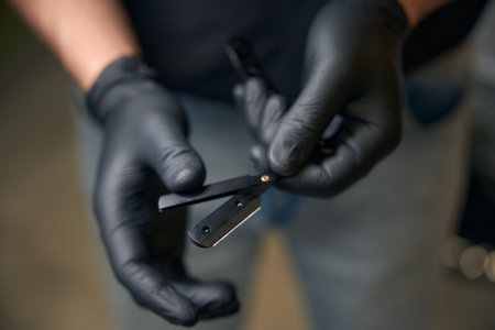 Barber in black gloves preparing razor for work in barbershopの写真素材