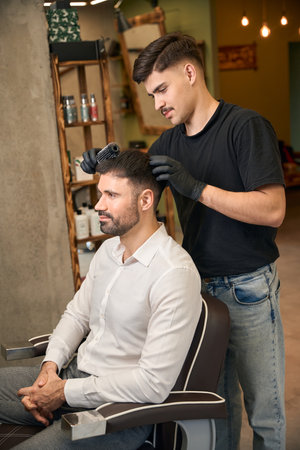 Coiffeur making new hairstyle for bearded customer in barbershopの写真素材