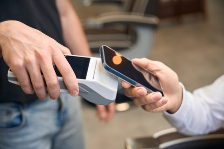 Male client making contactless paying with smartphone on pos terminal