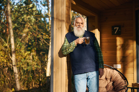 Old man enjoys a cup of tea on veranda of country houseの写真素材