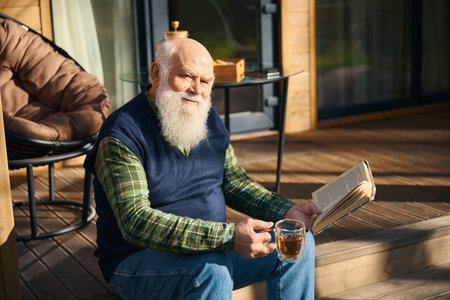 Cute old man sitting with a book on the porchの写真素材