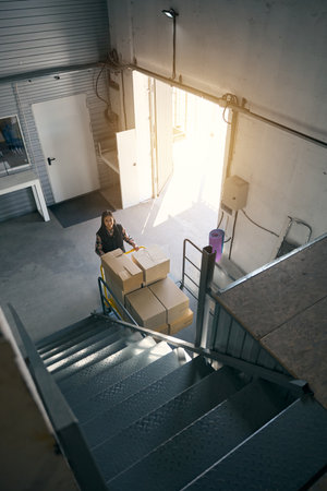 Joyous loader transporting wares on wheeled cart in warehouse