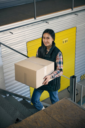 Joyous young storehouse worker carrying cargo upstairs