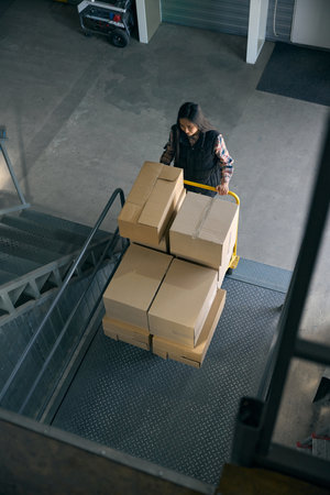 Freight handler transporting goods on wheeled cart in warehouse facilityの写真素材