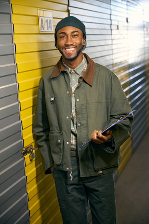 Smiling African man stands in storage service and holds a folder in his handsの写真素材