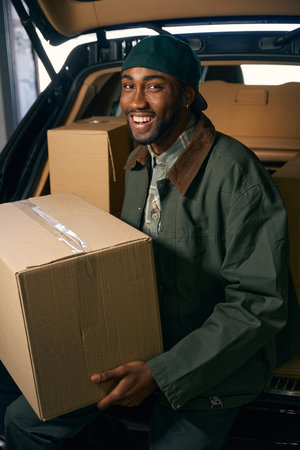 Smiling young male is sitting in the trunk of a auto, holding a box in his handsの写真素材