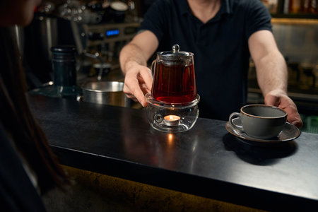 Bartender preparing one cup with saucer and teapot with freshly brewed teaの写真素材