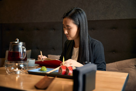 Creative young woman making notes in her notebook at japanese restaurantの写真素材