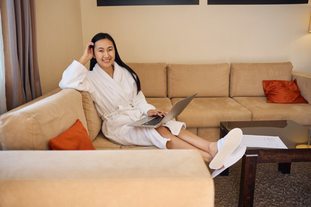 Joyous young woman whiling away time with laptop at homeの写真素材