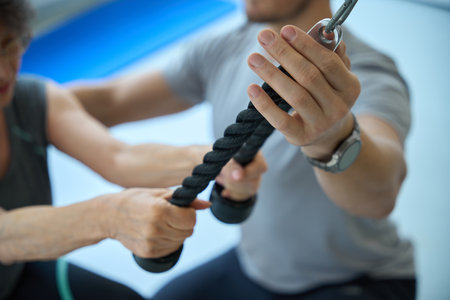 Young man helps an elderly woman do exercises on machineの写真素材
