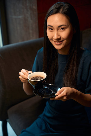 Asian woman enjoying fragrance and taste of coffee in restaurantの写真素材