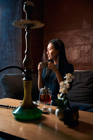East Asian woman resting in lounge hookah bar drinking teaの写真素材