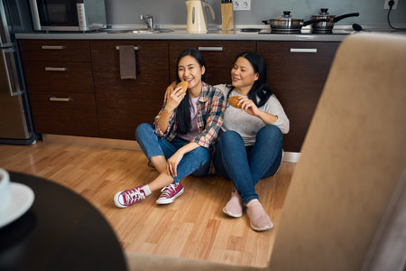 Smiling daughter and mother eating pastry at homeの写真素材