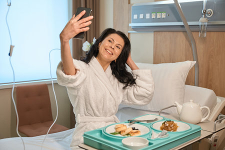 Lady takes selfie at breakfast in modern hospital wardの写真素材