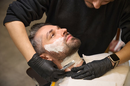 Barber applying shaving cream on clients neck and follow by straight razorの写真素材