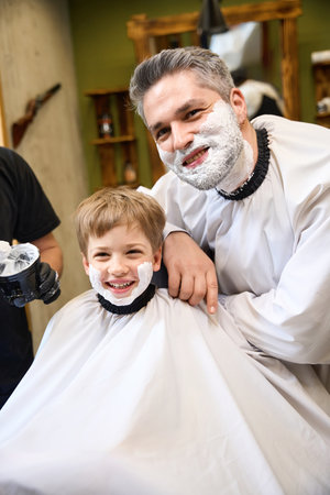 Father and son with shaving cream on their faces looking at cameraの写真素材