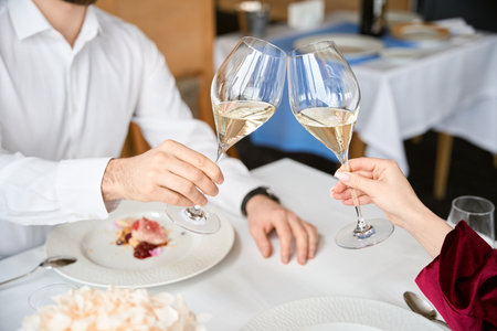 Cropped photo of couple clinking glasses of white wine in the restaurantの写真素材