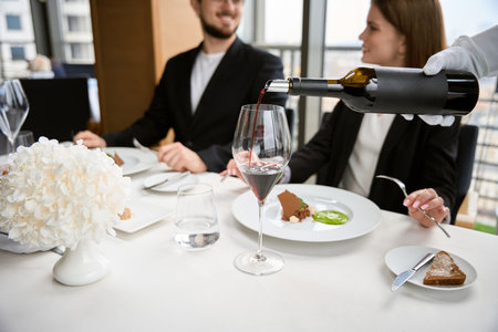 Happy couple talking and sitting in restaurant, while waiter pouring wineの写真素材