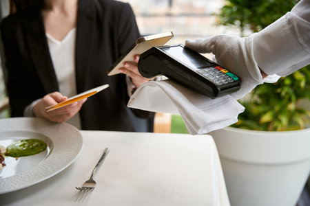 Young woman paying bill using mobile phone with NFC technology in restaurant