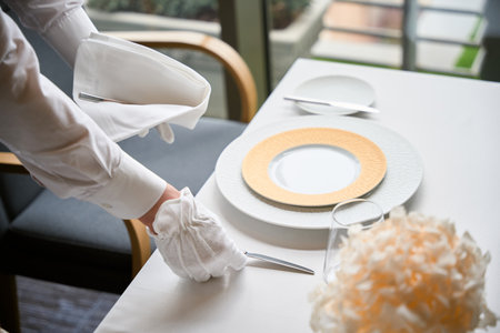 Cropped photo of waiter hand arranging cutlery on restaurant tableの写真素材