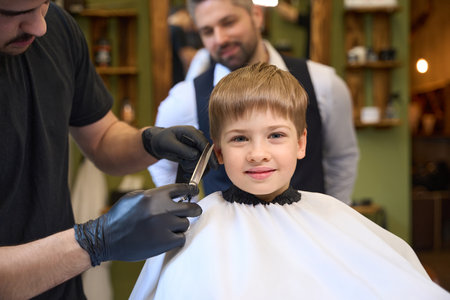 Pretty little boy looking experienced barber cutting hair above his earsの写真素材