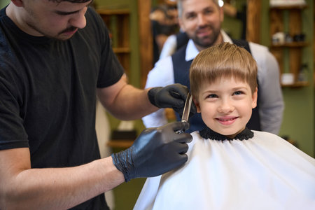 High qualified barber cutting excess hair above little client earsの写真素材